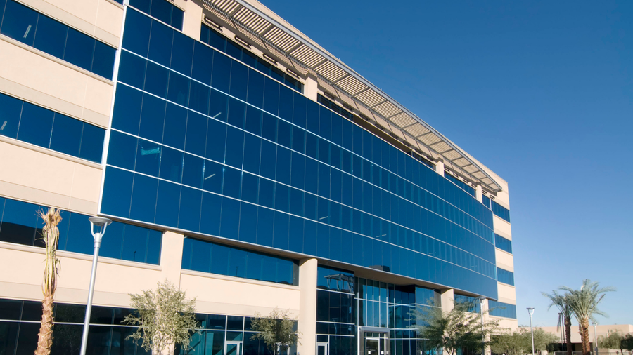 Modern blue glass office building with white accents and a reflective facade under a clear sky