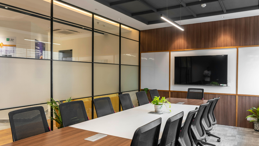 Modern conference room with long wooden table, black chairs, glass partition, and wall-mounted TV