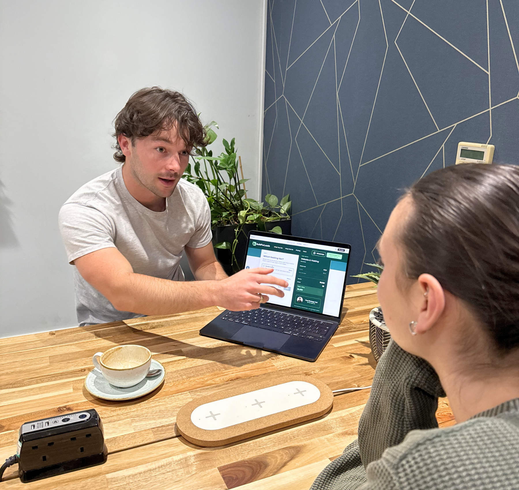 Two people discussing a laptop at a wooden table in a cafe