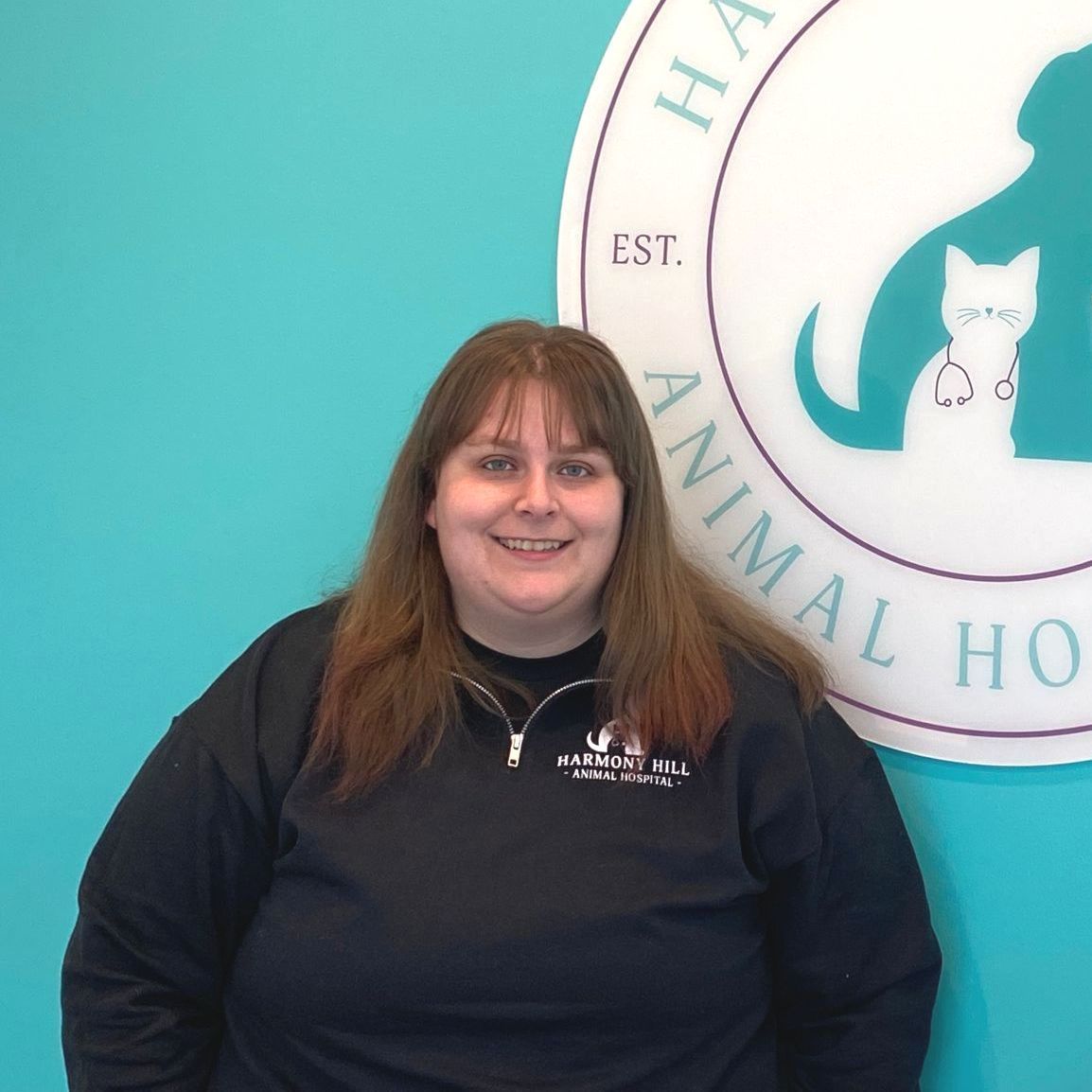 A woman stands in front of a sign for harmony hill animal hospital