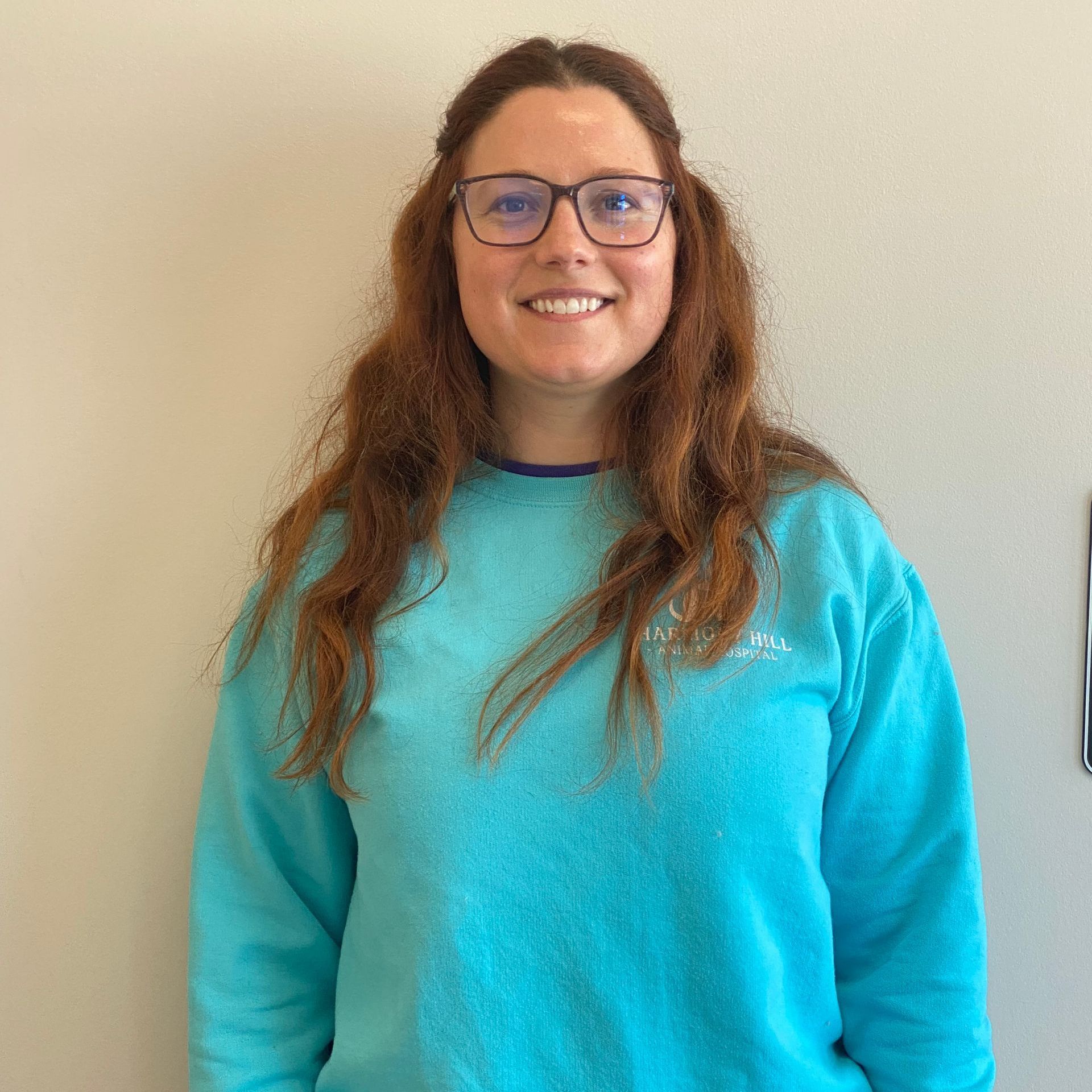 A woman wearing glasses and a blue sweater is smiling for the camera.