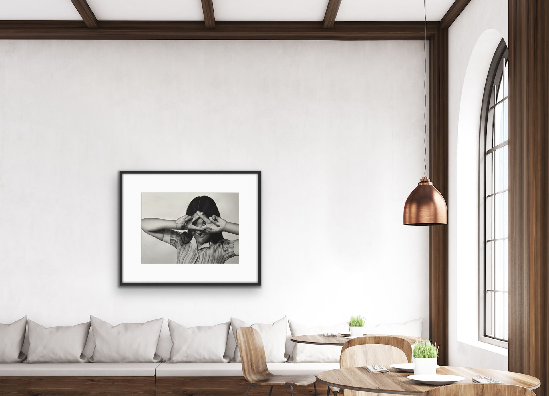 Minimal living room with a long sofa, framed wall art, wooden beams, and a copper pendant lamp by a large window