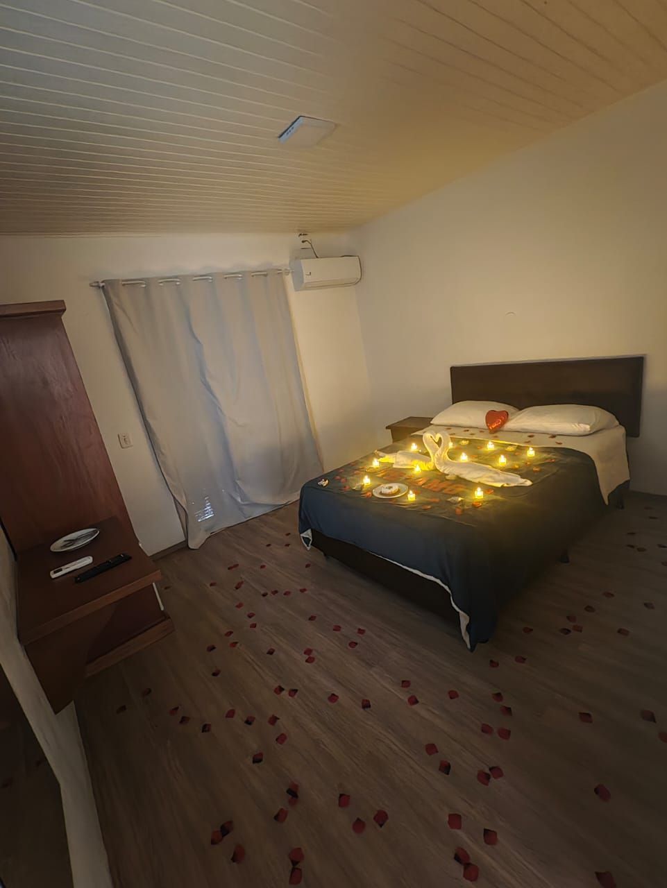 Quarto com cama iluminada por luzes de cordão em tons quentes, cortinas, guarda-roupa e tapete estampado.