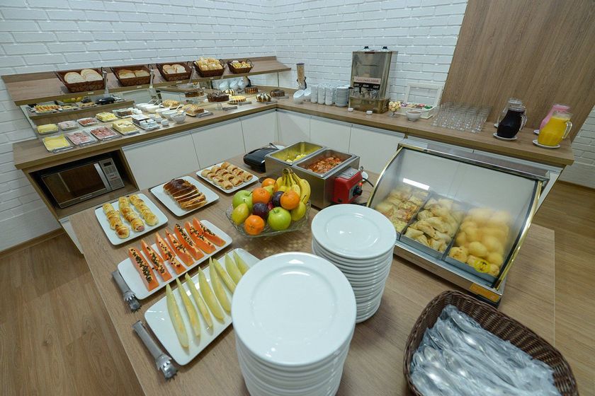 Buffet self-service com doces, frutas, sanduíches e pilhas de pratos em um balcão.