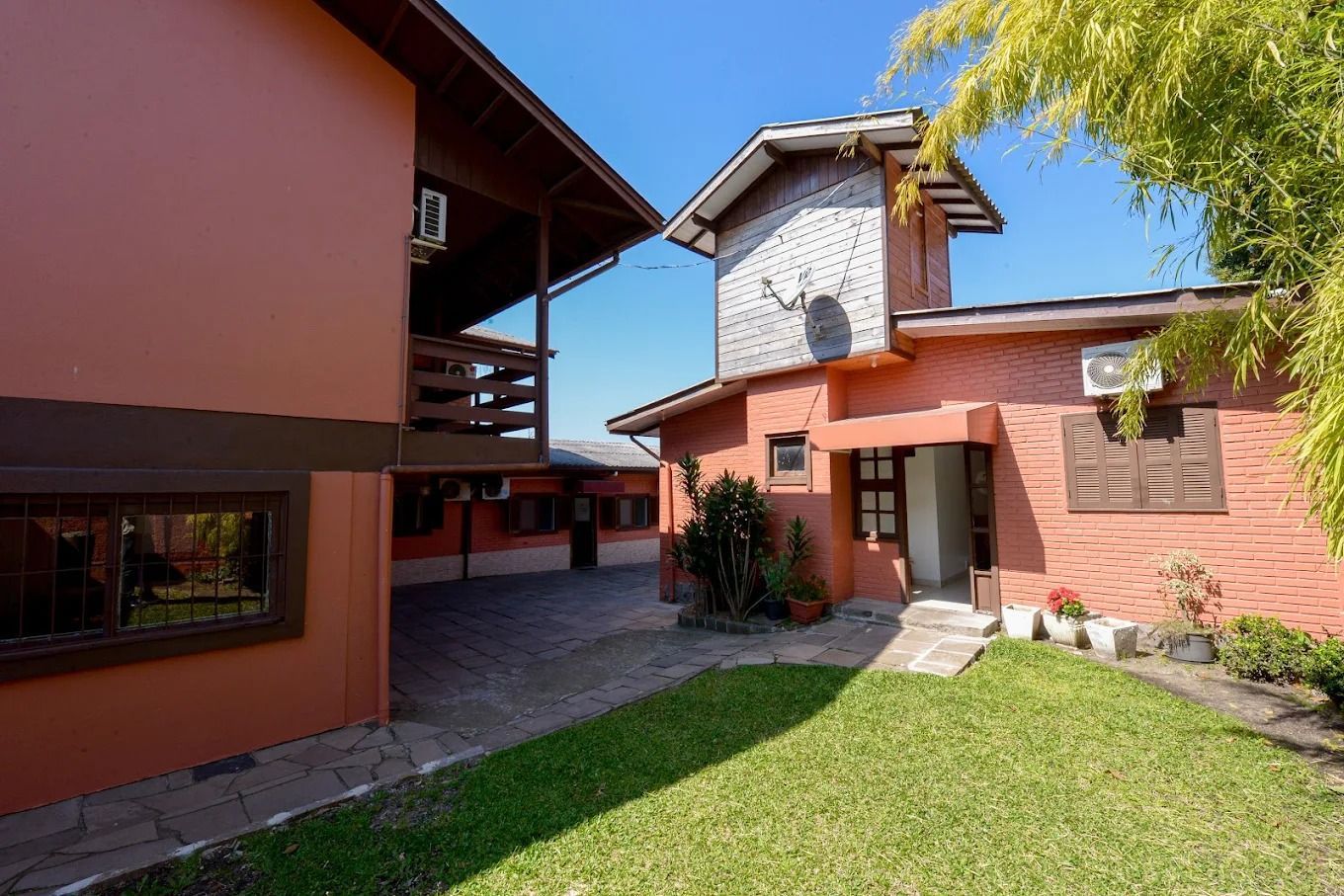 Pátio entre prédios vermelhos com gramado verde e céu azul.