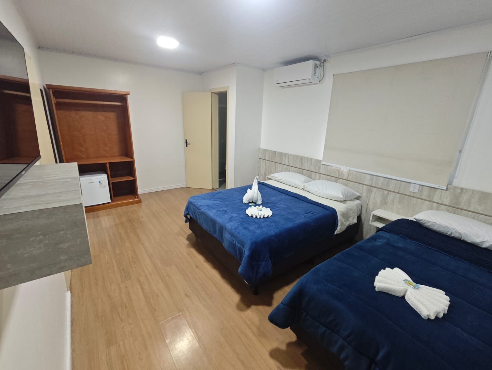 Duas camas de solteiro com lençóis azuis em um quarto de hotel luminoso e minimalista.