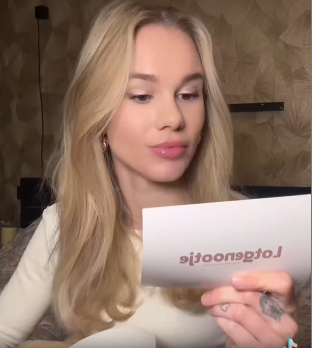 Een persoon met blond haar houdt een witte kaart vast met het woord