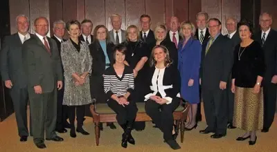 Group portrait of formally dressed people posing indoors in front of a curtain backdrop