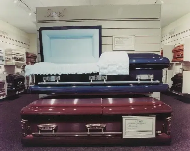 Two coffins displayed in a funeral home showroom, one white and one burgundy.