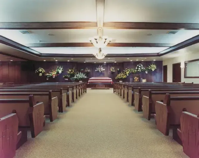 Empty church interior with wooden pews, central aisle, and floral decorations near the altar