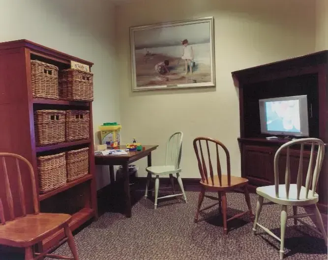 Cozy room with wicker storage shelves, two chairs, small desk, and TV cabinet on carpeted floor.