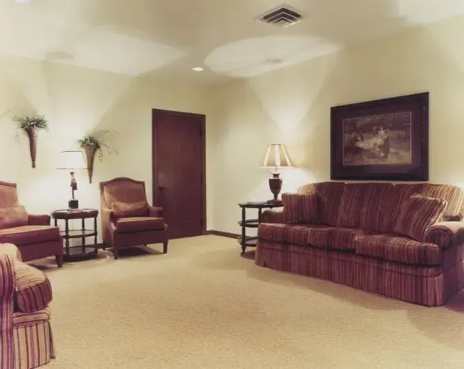 Waiting room with two armchairs, a maroon sofa, side tables, lamps, and beige carpet under soft lighting