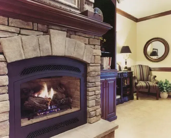 Cozy living room with a stone fireplace burning beside a carpeted seating area and lamp.