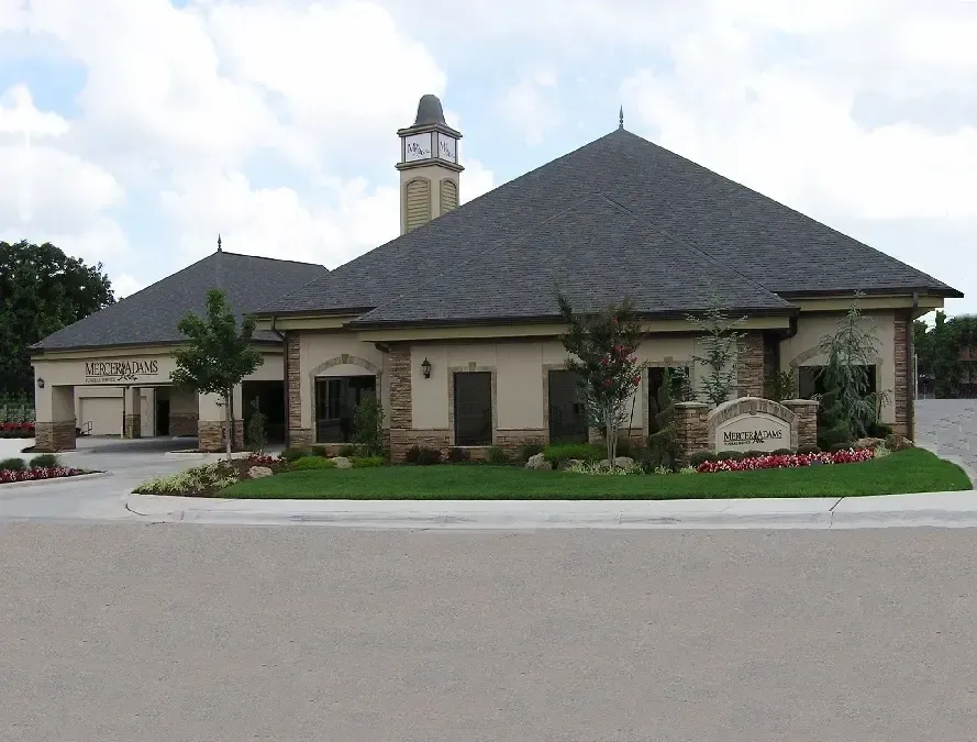 Single-story beige building with a dark roof and cupola, landscaped entrance, and curved driveway.