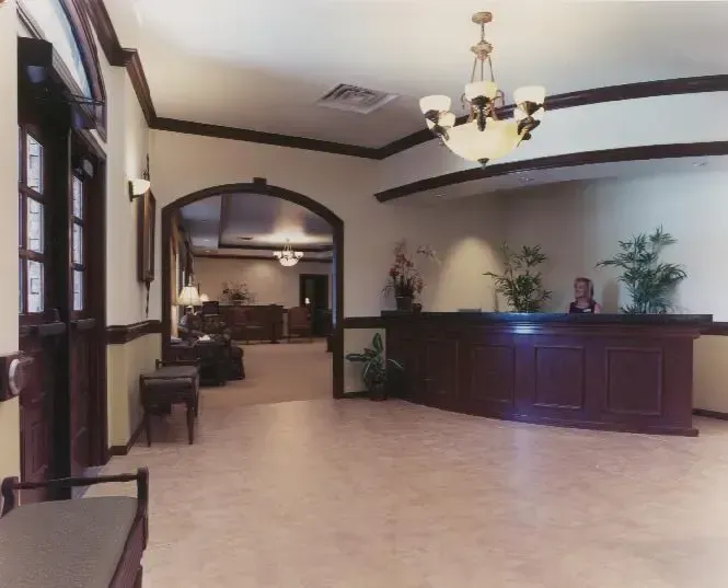 Hotel lobby with beige tile floor, dark wood reception desk, arched doorway, and chandelier lighting