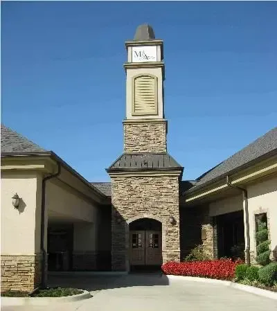 Brick apartment building entrance with central tower, blue sky, and red flowers