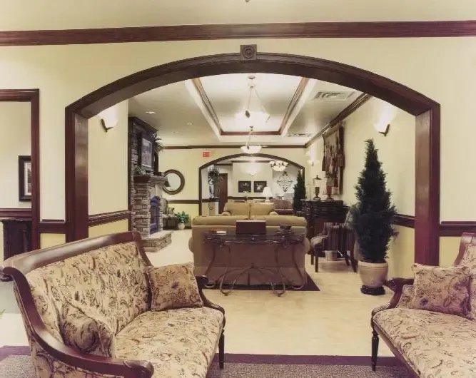 Elegant lobby with upholstered chairs, a central table, and an arched doorway leading to a mirrored room.
