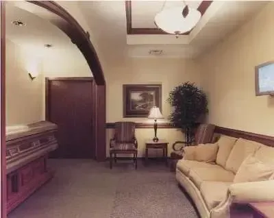 Dim hotel lobby with beige sofa, armchairs, table lamp, and framed wall art.