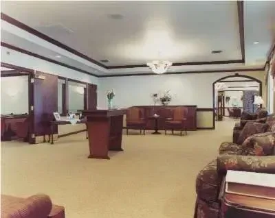Empty hotel lobby with beige carpet, wooden podium, and patterned chairs near a front desk area