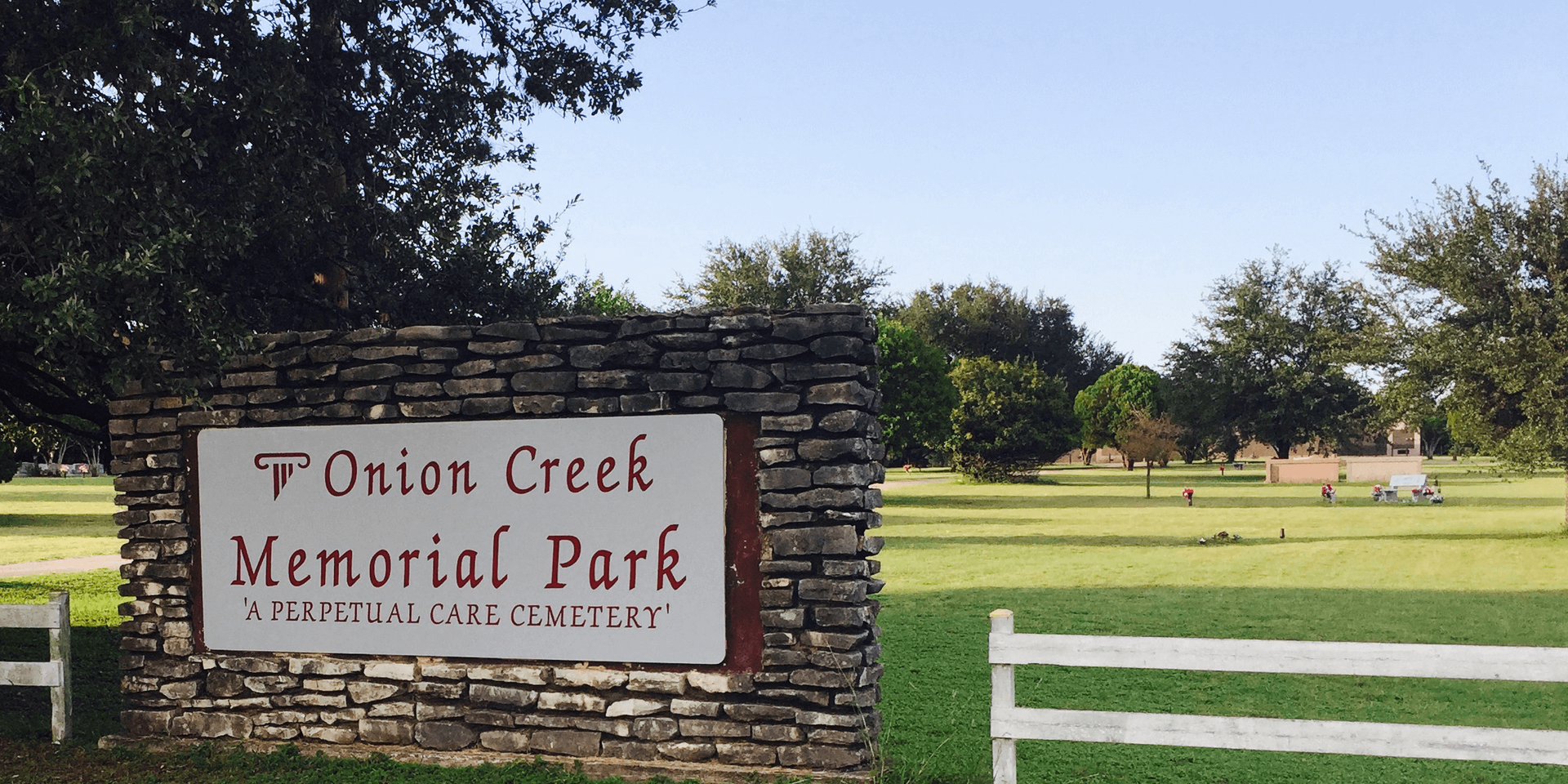 Stone sign for Onion Creek Memorial Park in a grassy park with trees and benches