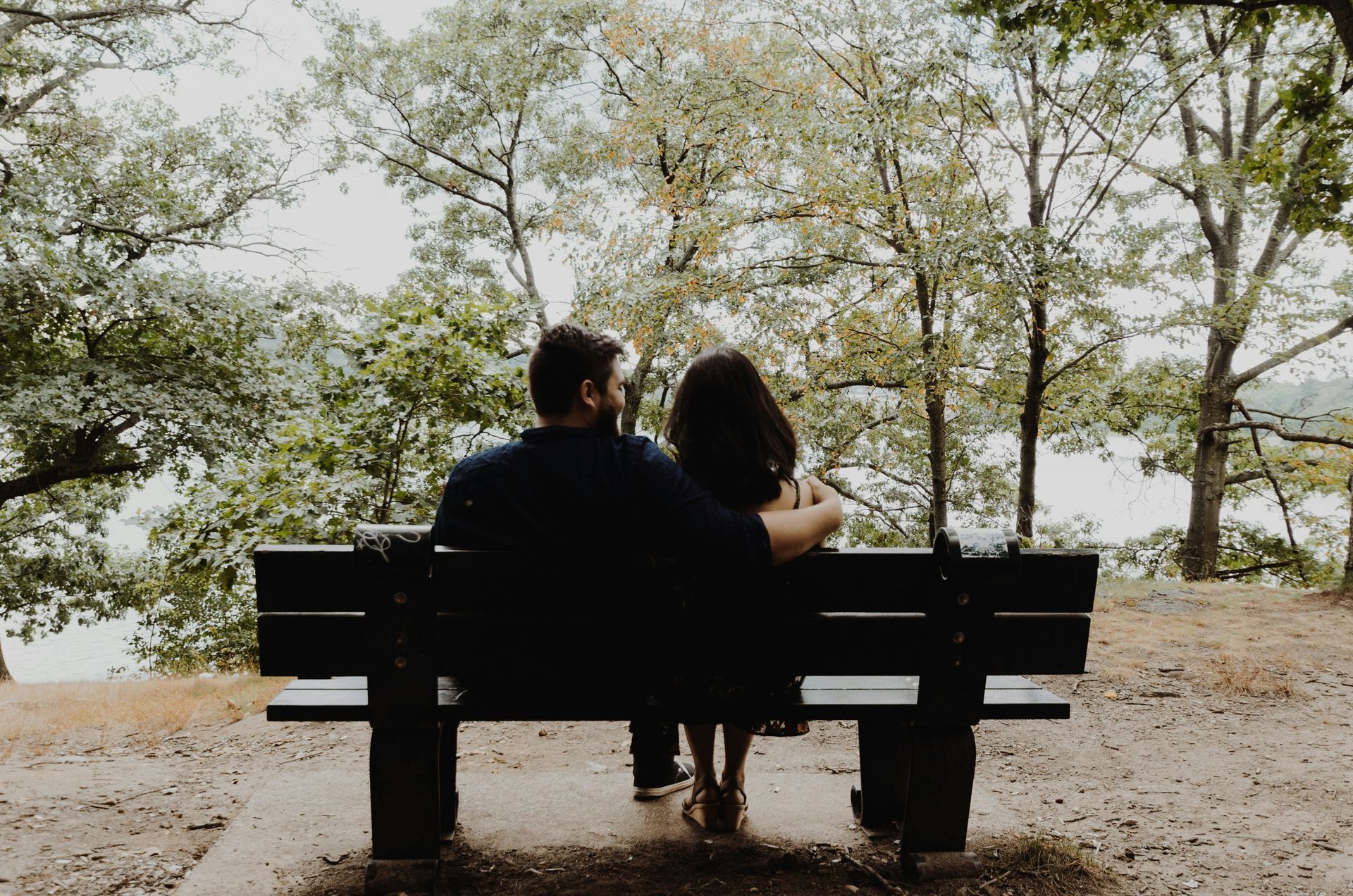 Couple sitting on a bench under trees, overlooking a calm lakeside scene