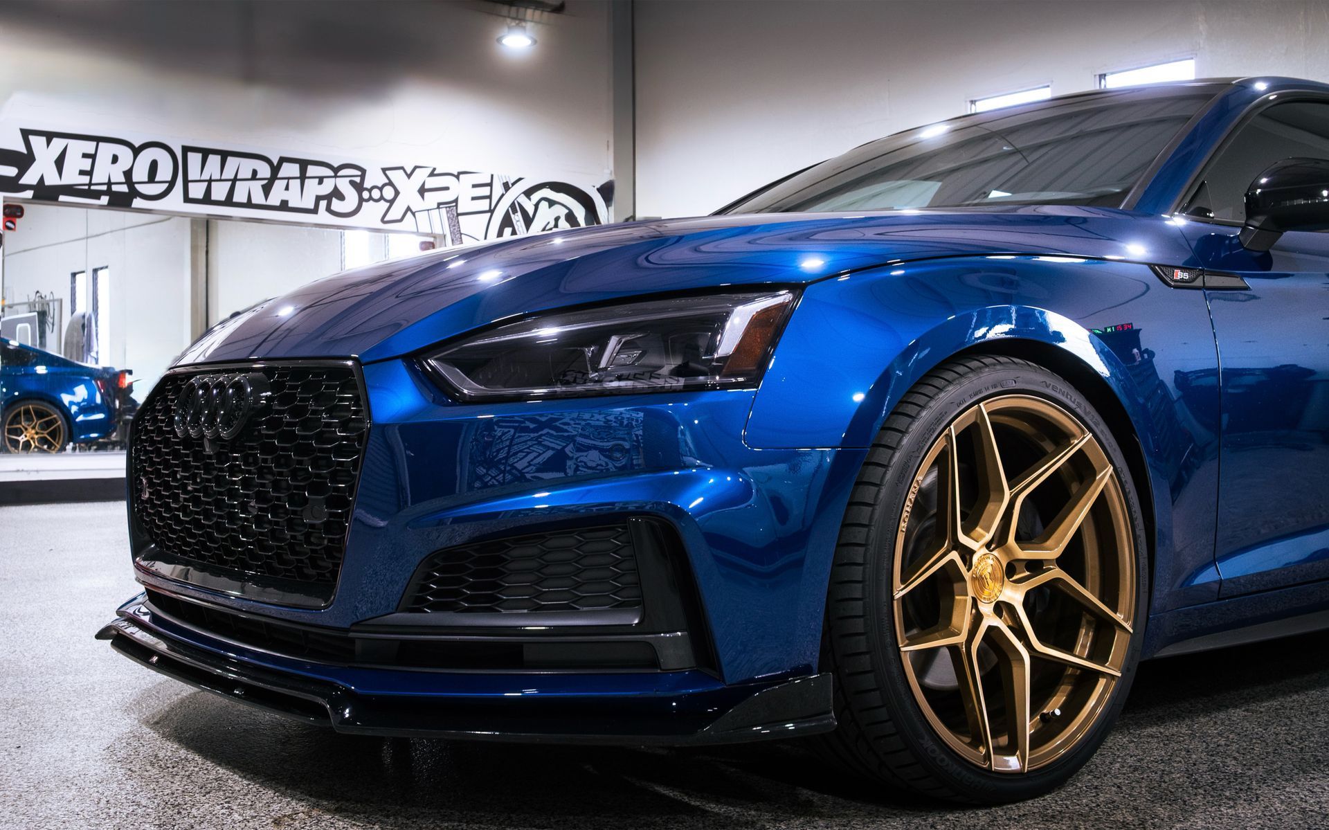 Blue sports car with gold rims displayed indoors at an auto shop show