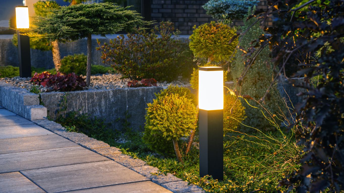 A sidewalk with a row of lights on it in a garden at night.