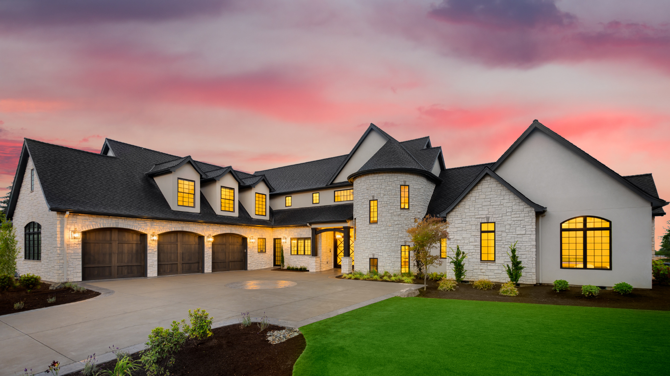 A large white house with a black roof is sitting on top of a lush green lawn.