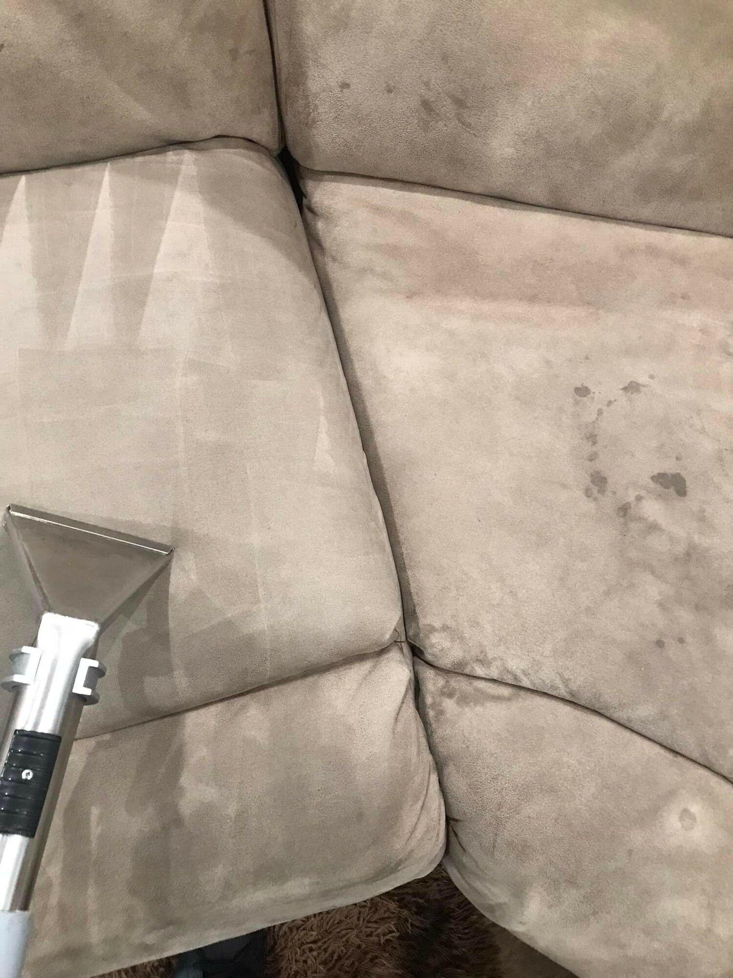 A person is cleaning a couch with a vacuum cleaner.