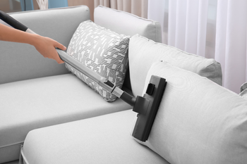 A person is cleaning a couch with a vacuum cleaner.