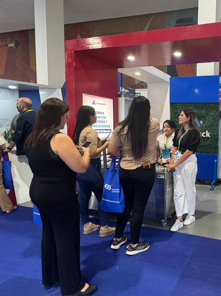 Personas reunidas en un stand de exhibición con una estructura roja y azul en una feria comercial.
