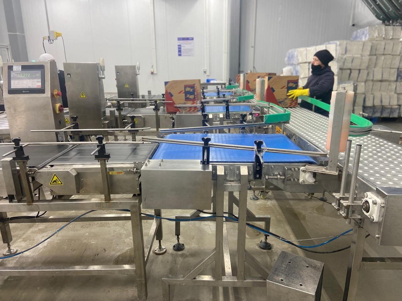 Cajas en una cinta transportadora en una fábrica, trabajador con máscara, maquinaria.