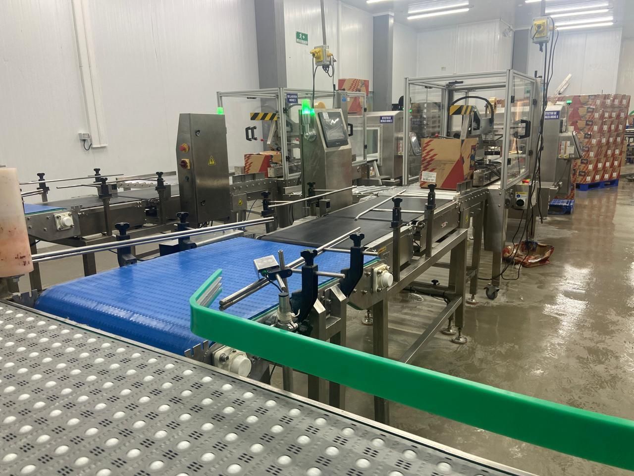 Línea de procesamiento industrial de alimentos con cintas transportadoras, maquinaria y cajas en una fábrica.