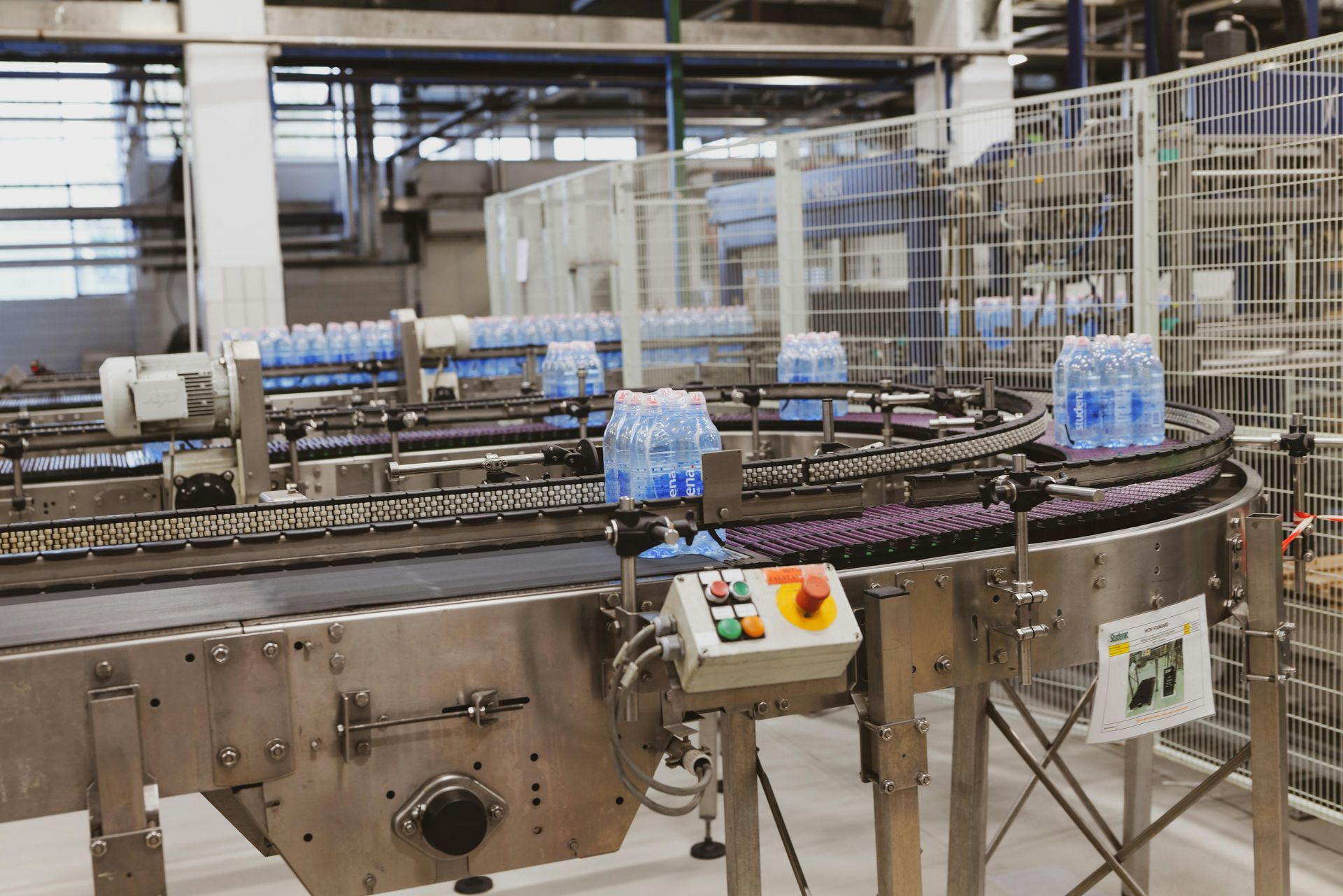 Agua embotellada en una cinta transportadora en un entorno de fábrica, maquinaria.