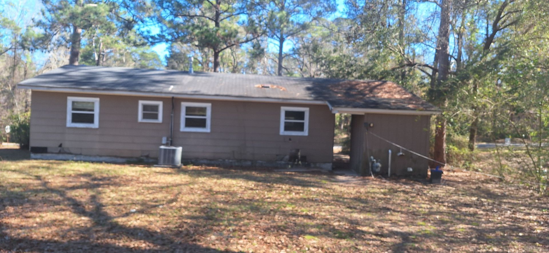 Single-story brown house with white-trimmed windows in a wooded yard.