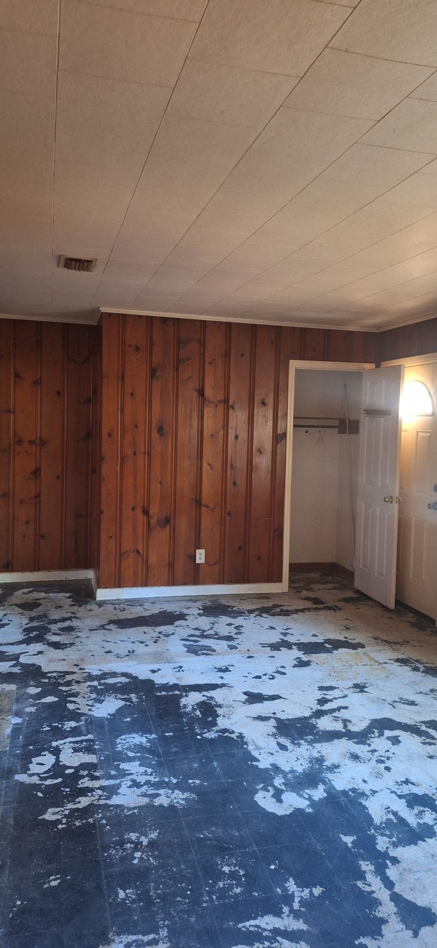 Empty room with wood-paneled wall, worn blue carpet, and open doorway to the right.