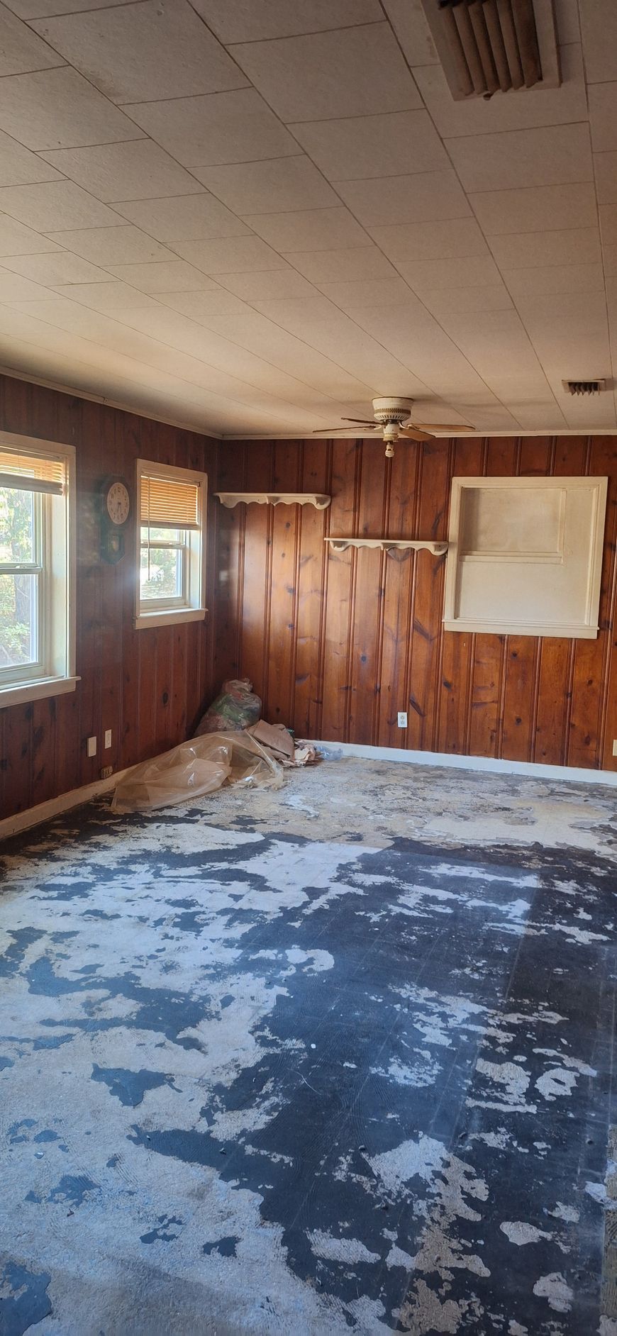 Abandoned room with peeling blue floor paint, wood-paneled walls, windows, and a whiteboard on the wall