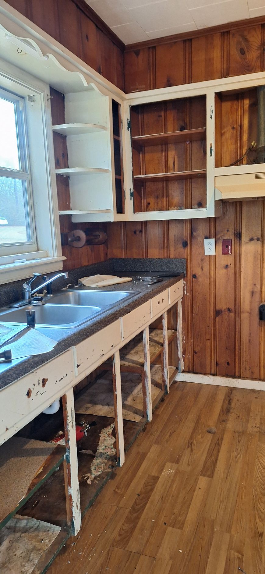 Partially renovated kitchen with wood-paneled walls, sink, open cabinets, and unfinished counter framing