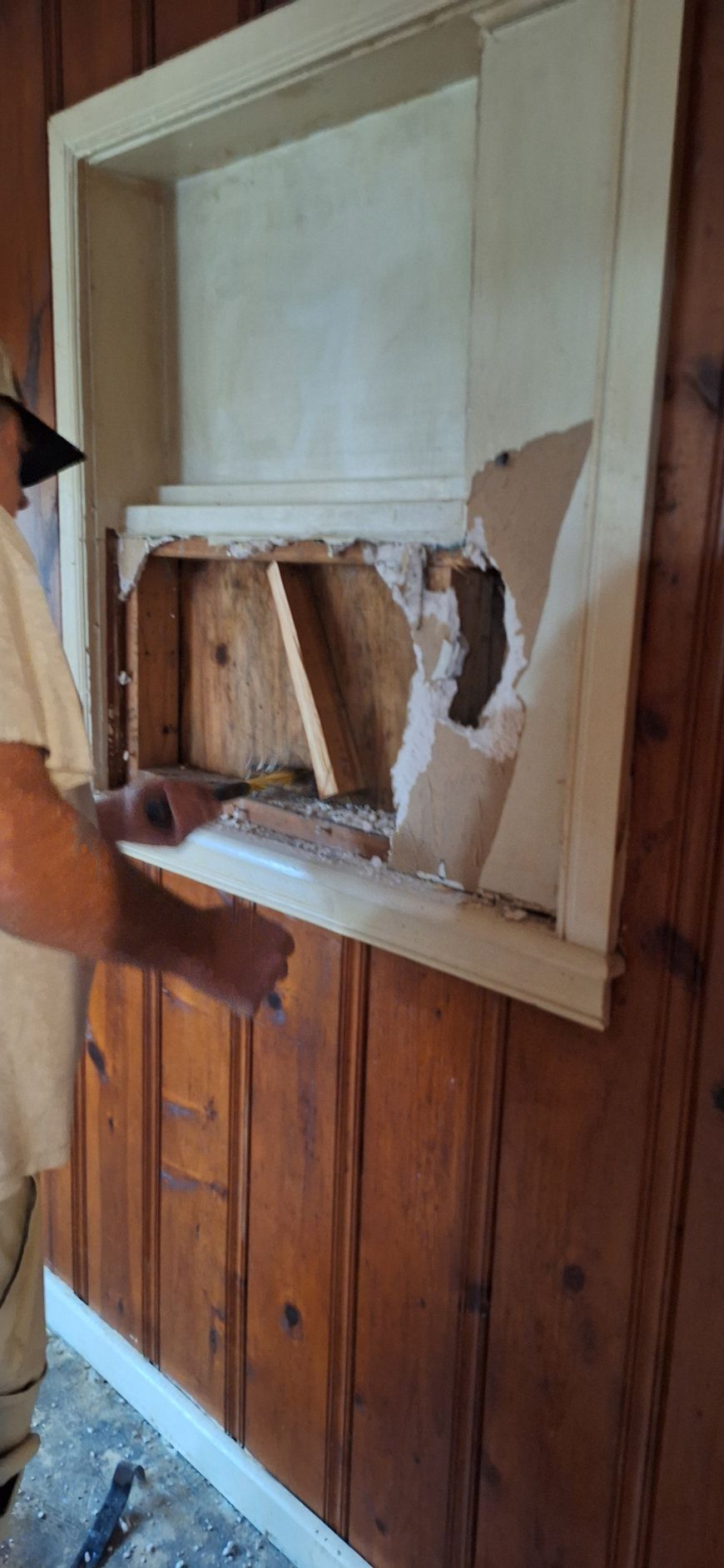 Damaged wall panel with torn plaster above wood wainscoting in an interior room