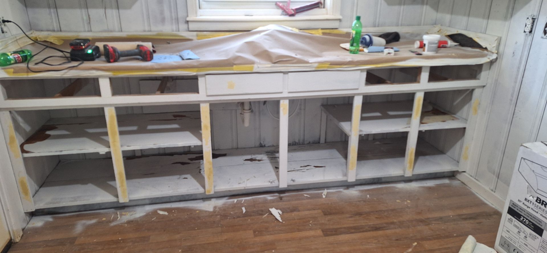 Partially renovated kitchen with unfinished white cabinets, tools, and a sink along the wall