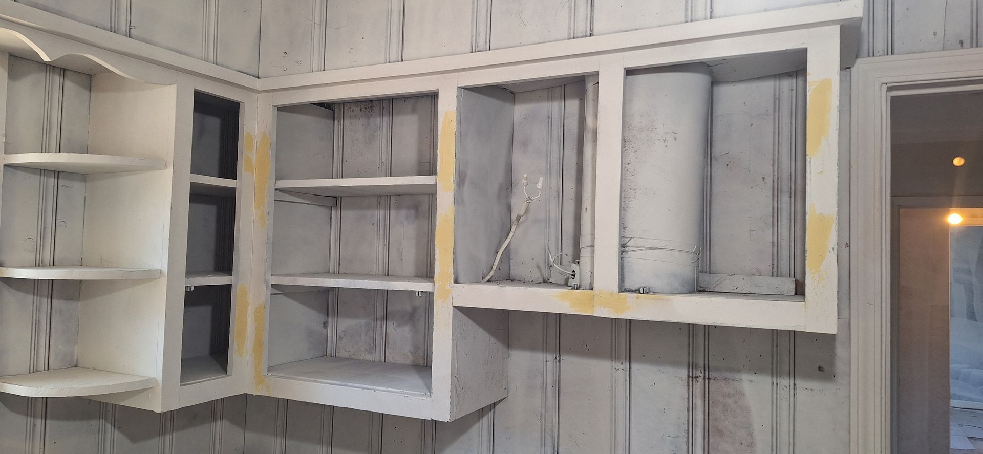 White built-in wall shelves and cabinets in a partially finished room with a doorway on the right.