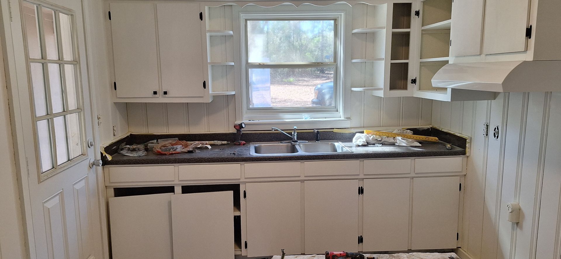 Small kitchen with white cabinets, black countertop, open upper cabinets, and a window above the sink.