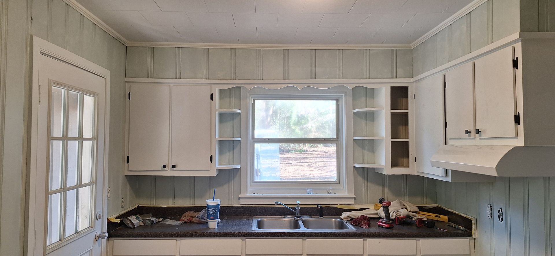 Small white kitchen with cabinets, window over sink, and countertops under construction or renovation