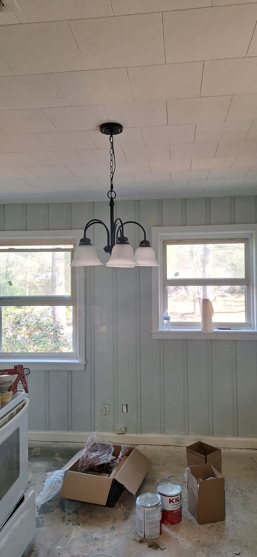 Renovated room with unfinished ceiling, hanging light fixture, and boxes and paint supplies on the floor