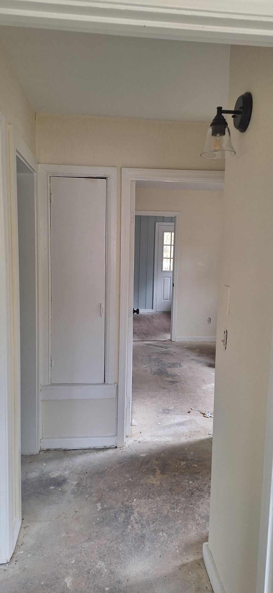 Narrow hallway with unfinished walls and debris, leading to a room with a window.
