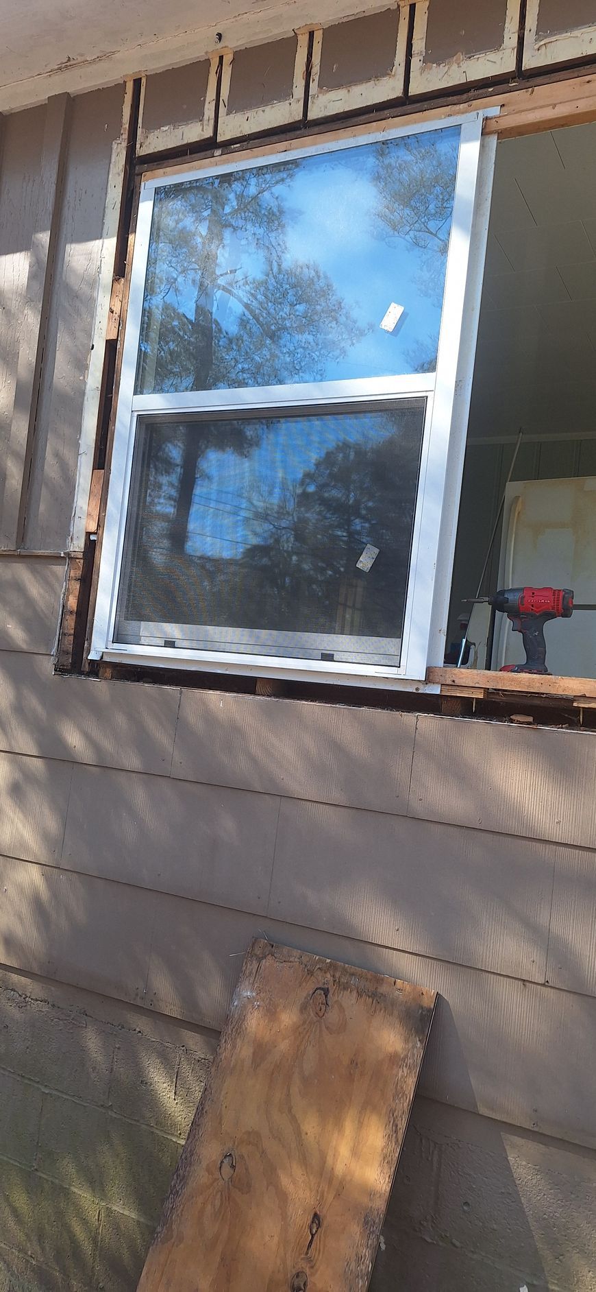 House window with white trim and a red flowerpot on the sill, seen from outside above a wood board.