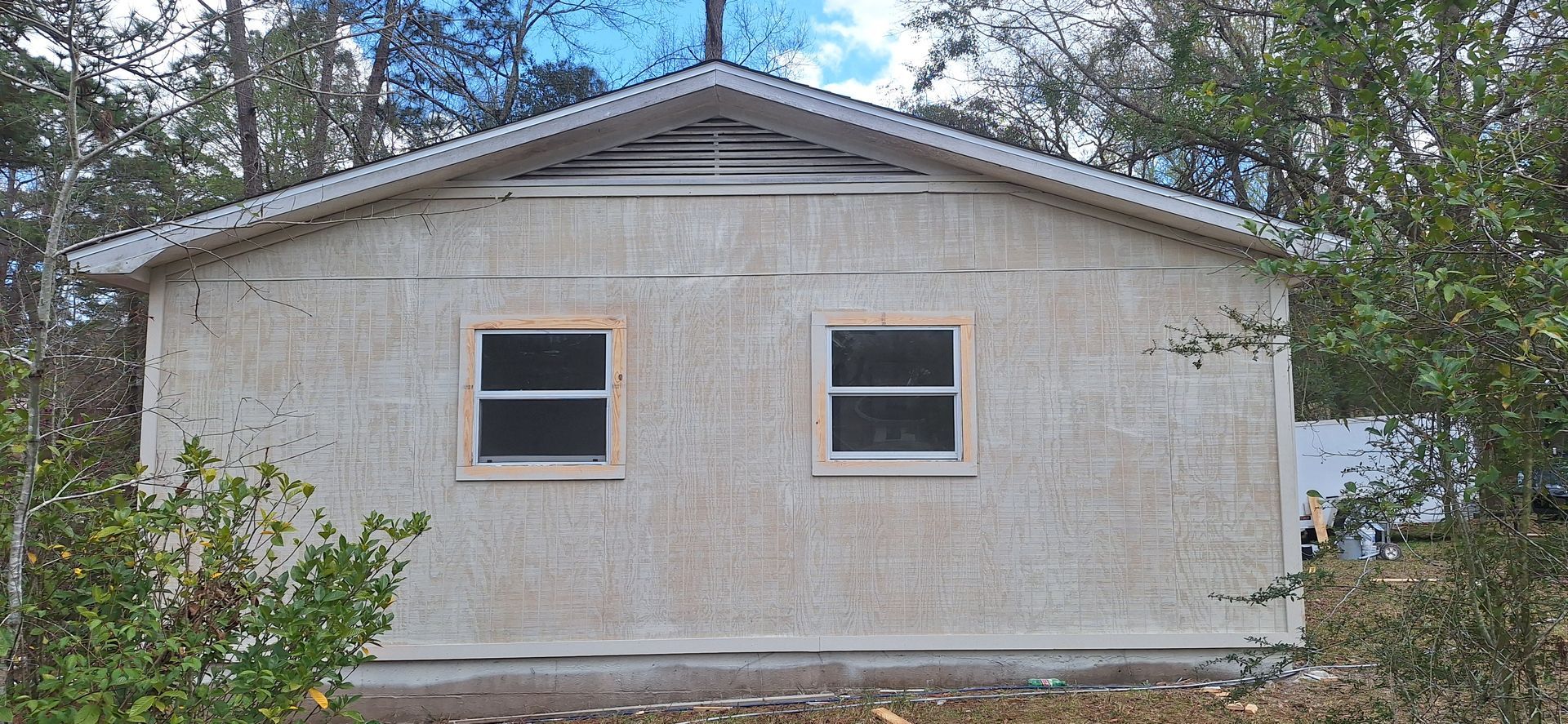 Front view of a small beige house exterior with two windows and a peaked roof