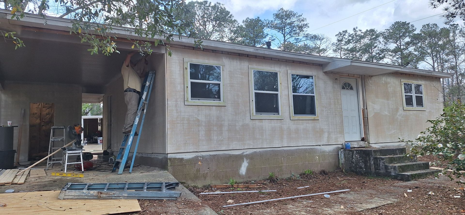 Partially renovated house with new windows, ladder, and construction materials outside