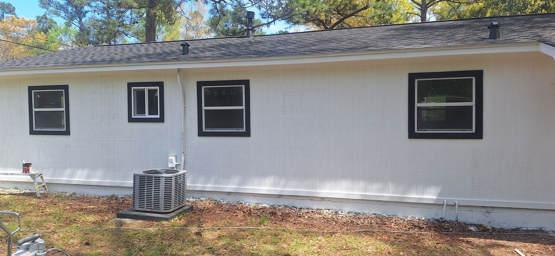 Single-story white house exterior with black-trimmed windows and an air conditioner unit in front