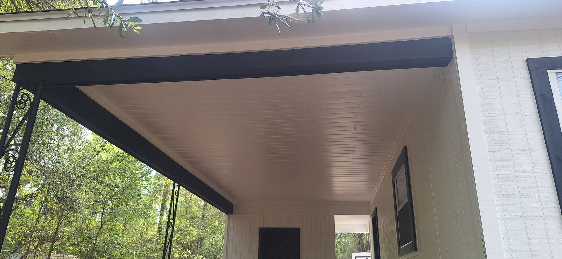 Covered porch with dark wood ceiling and white siding on a house, viewed from below.